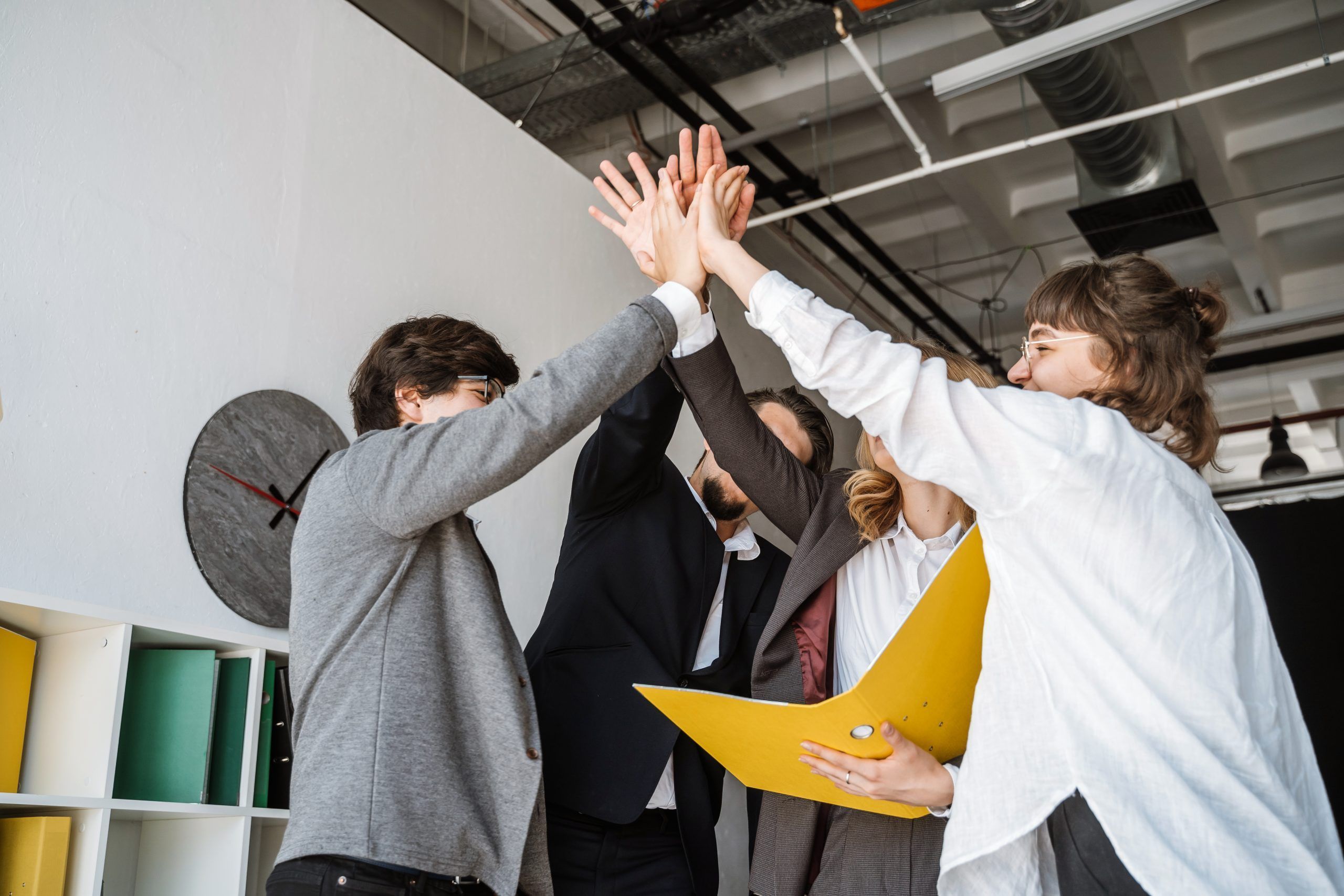 Cheerful young group of people standing in the office and giving high five 1 scaled 1
